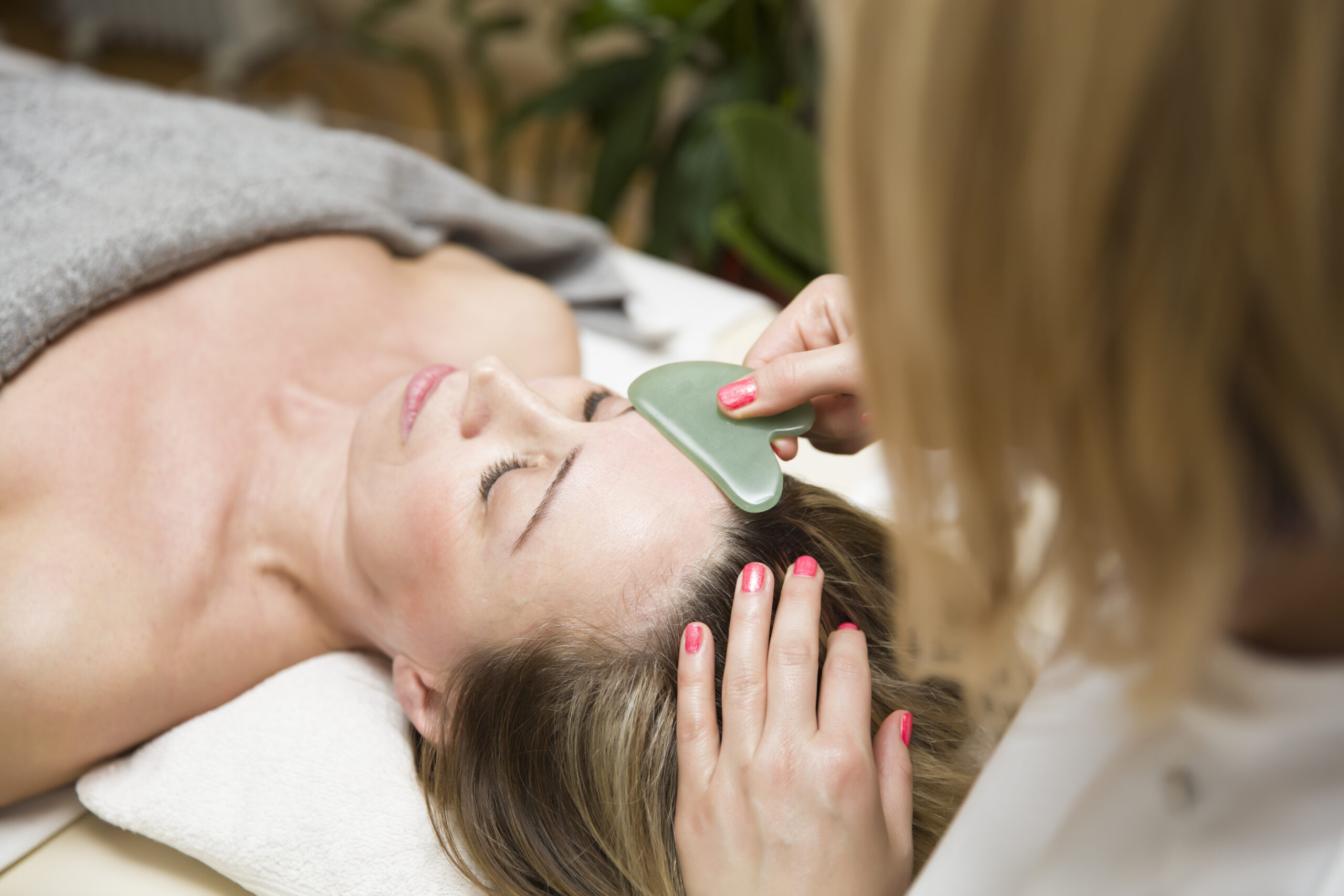 Woman having an gua sha facial massage with natural jade stone m